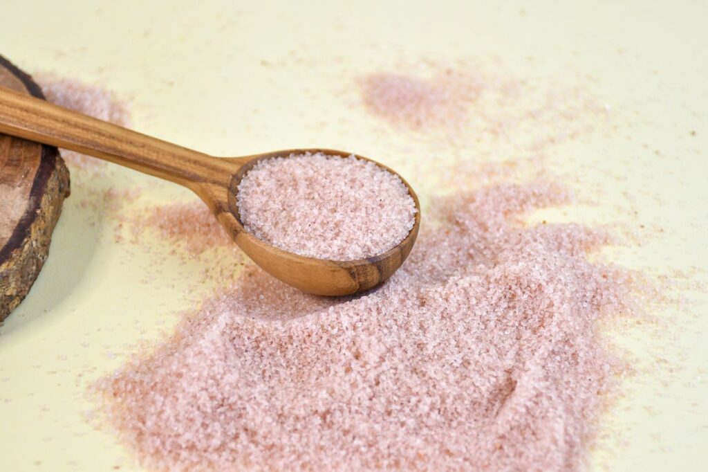 Close-up of pink Himalayan salt in a wooden spoon on a yellow background, highlighting texture.