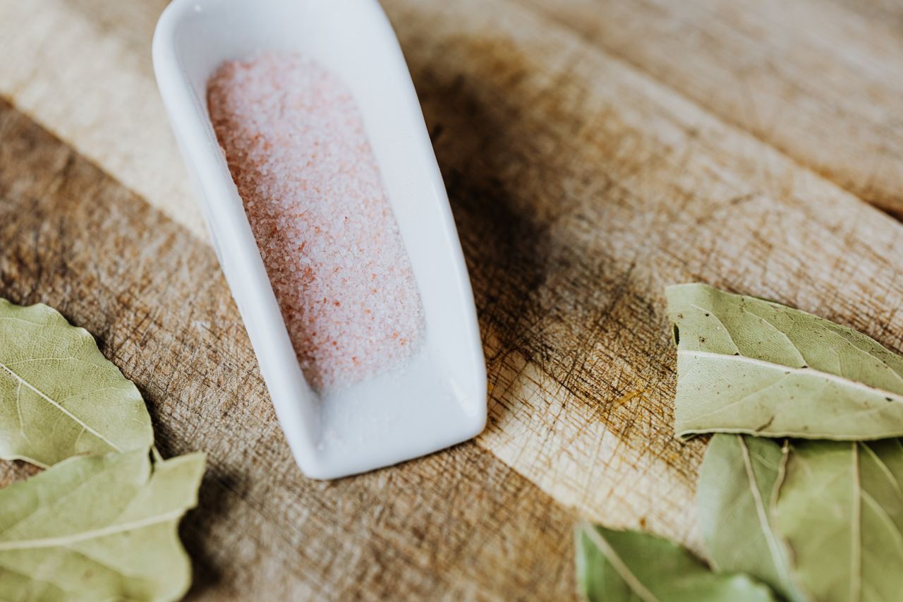 Close-up of pink Himalayan salt and bay leaves on a rustic wooden surface, highlighting natural ingredients.